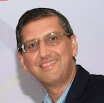 Rahul Mehta wearing dark jacket, light blue shirt and eyeglasses.